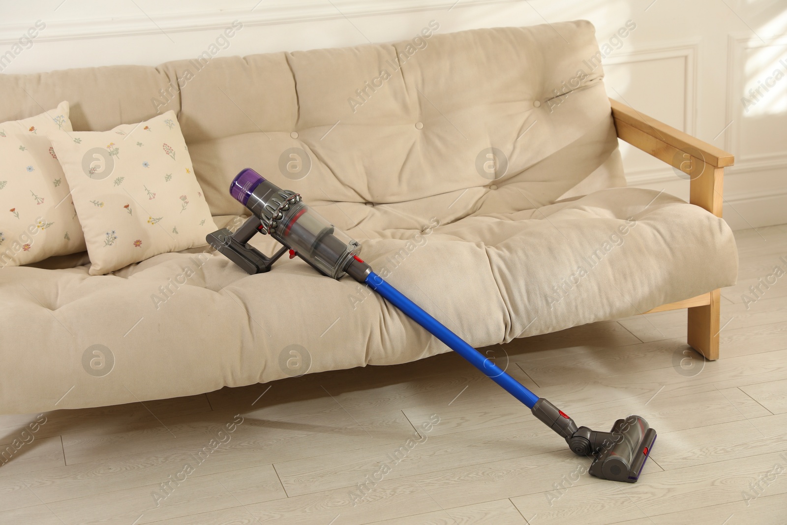 Photo of One cordless vacuum cleaner leaning on sofa indoors