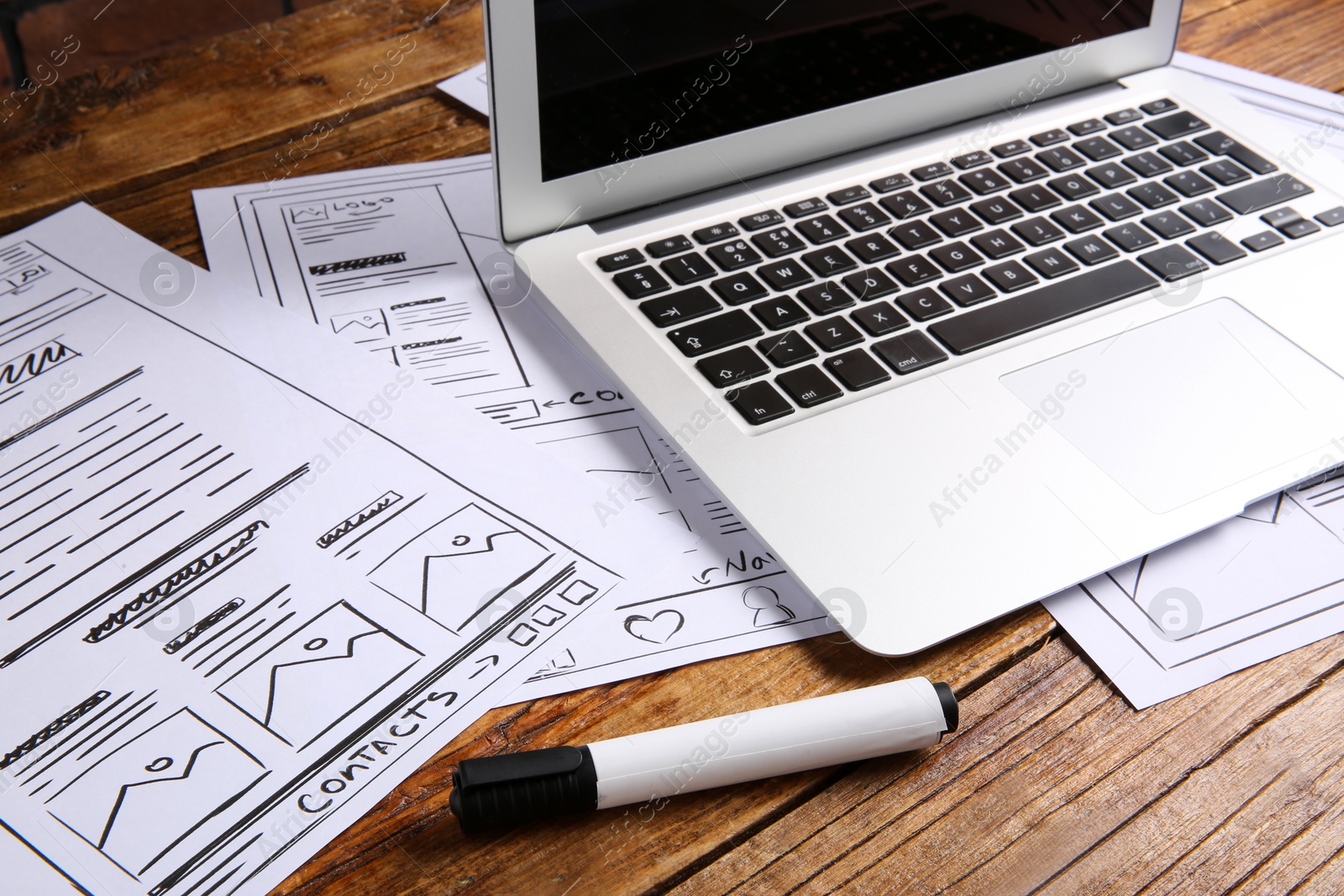 Photo of Developing UI design. Sketches of website wireframes, laptop and felt pen on wooden table, closeup