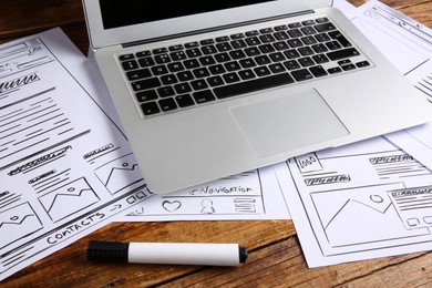 Photo of Developing UI design. Sketches of website wireframes, laptop and felt pen on wooden table, closeup