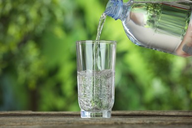 Photo of Pouring soda water in glass at wooden table outdoors