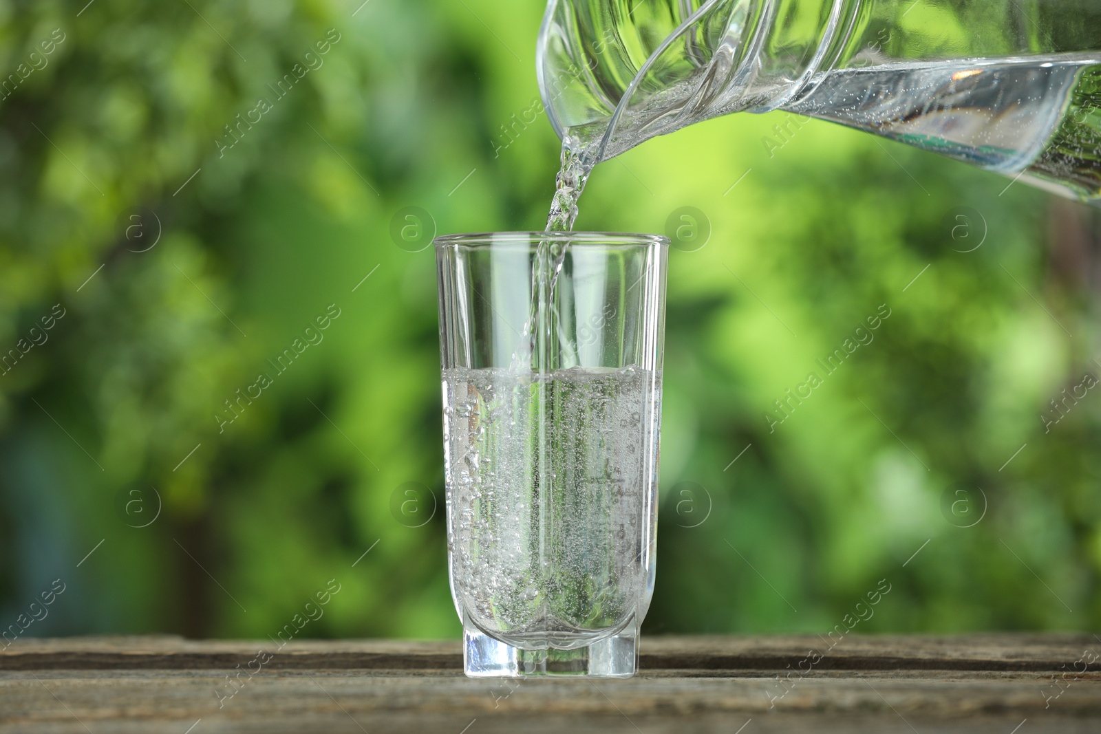 Photo of Pouring soda water in glass at wooden table outdoors