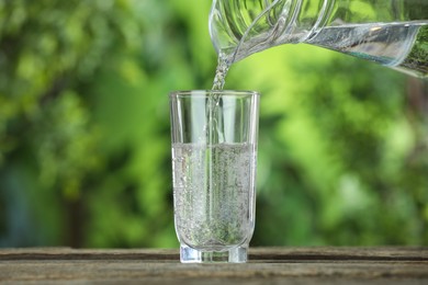 Photo of Pouring soda water in glass at wooden table outdoors