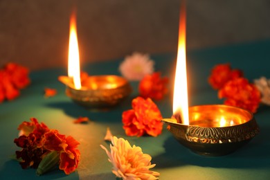 Photo of Diwali celebration. Diya lamps and beautiful flowers on teal table, closeup