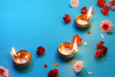 Diwali celebration. Diya lamps and beautiful flowers on blue background, flat lay. Space for text