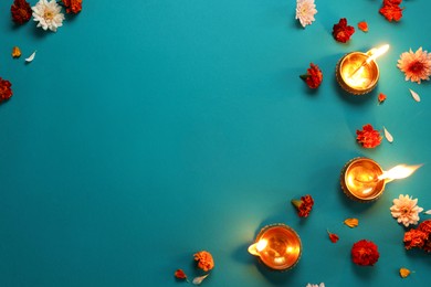 Photo of Diwali celebration. Diya lamps and beautiful flowers on teal background, flat lay. Space for text