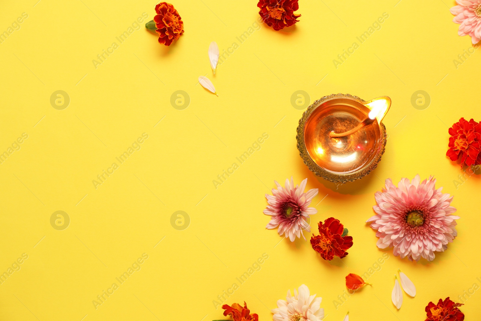 Photo of Diwali celebration. Diya lamp and beautiful flowers on yellow background, flat lay. Space for text