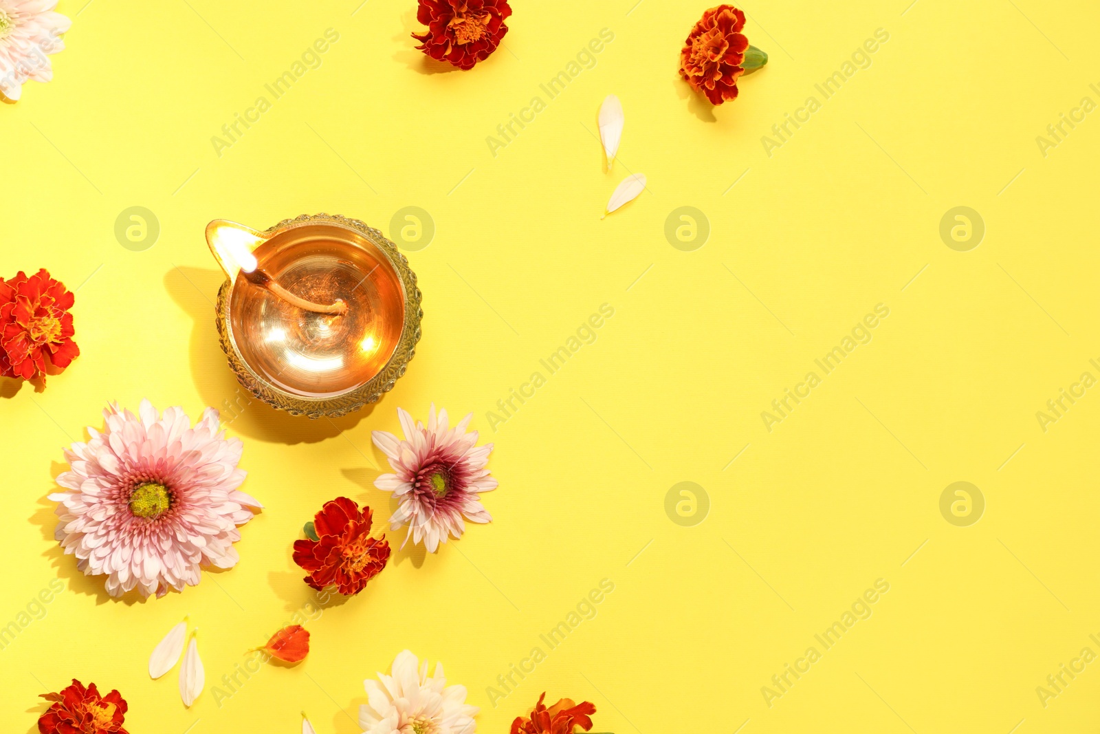 Photo of Diwali celebration. Diya lamp and beautiful flowers on yellow background, flat lay. Space for text