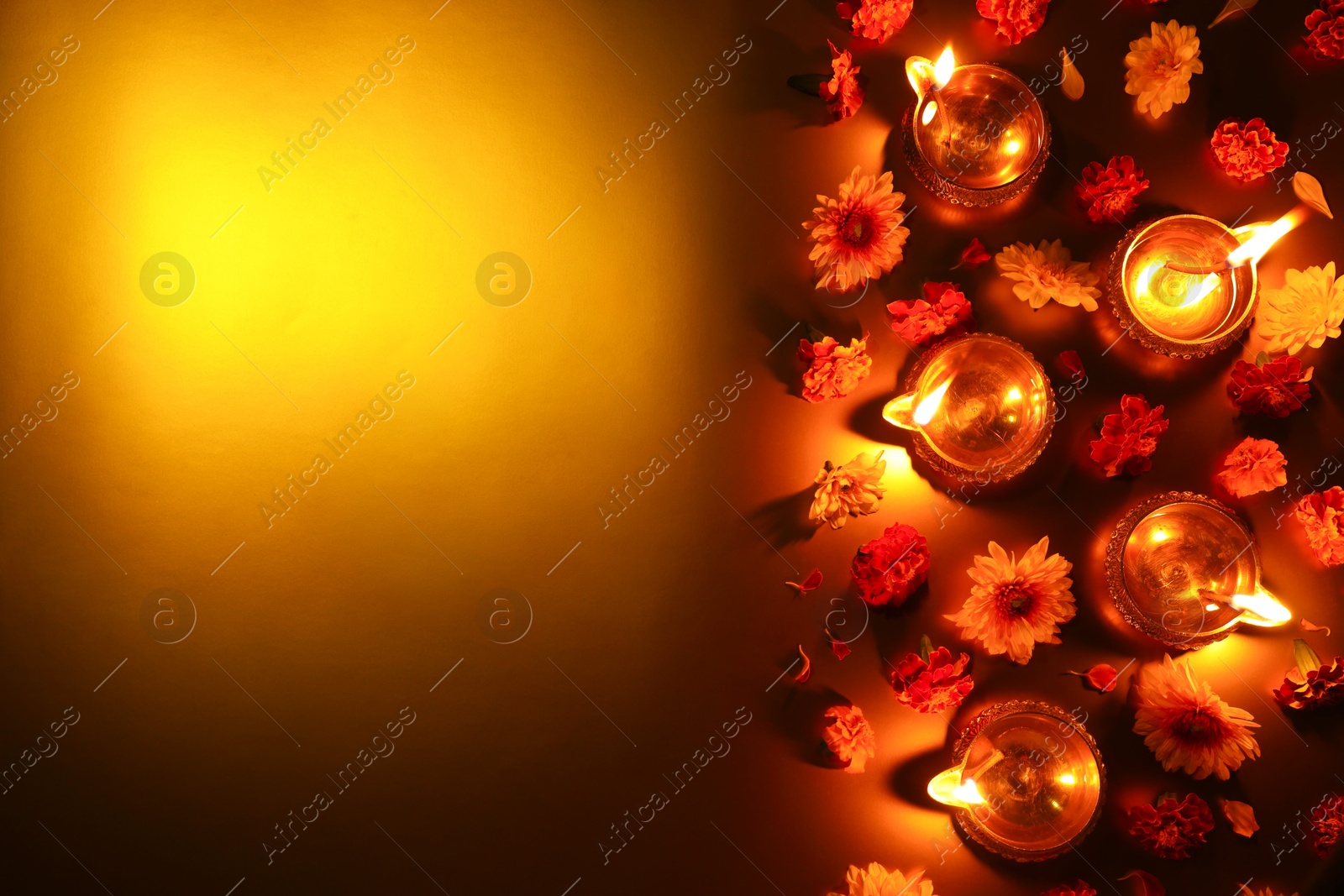 Photo of Diwali celebration. Diya lamps and beautiful flowers on golden background, flat lay. Space for text