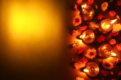 Photo of Diwali celebration. Diya lamps and beautiful flowers on golden background, flat lay. Space for text