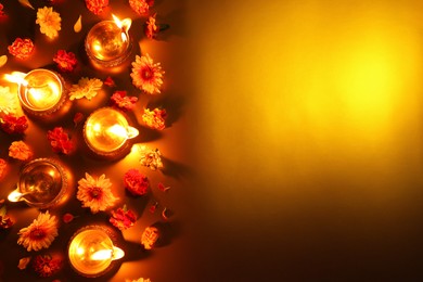 Photo of Diwali celebration. Diya lamps and beautiful flowers on golden background, flat lay. Space for text