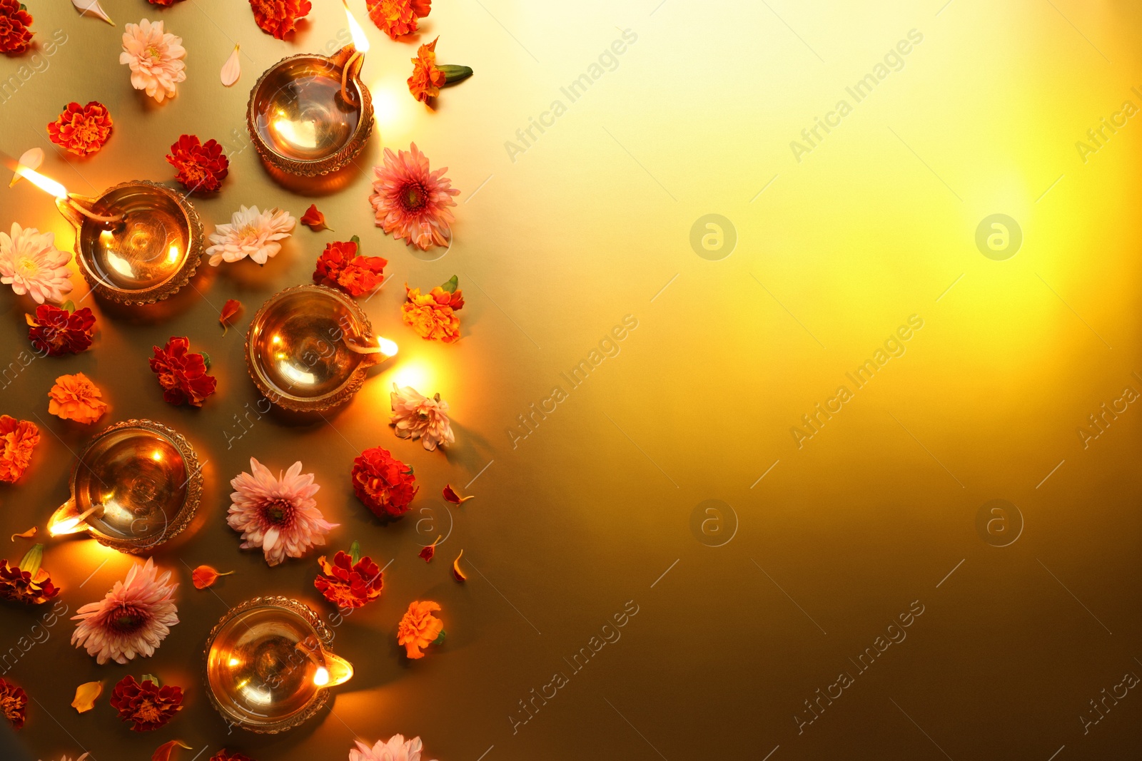 Photo of Diwali celebration. Diya lamps and beautiful flowers on golden background, flat lay. Space for text