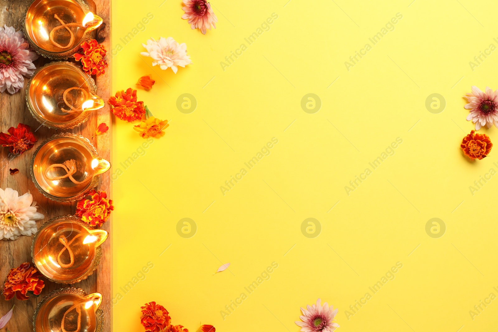 Photo of Diwali celebration. Diya lamps and beautiful flowers on yellow background, flat lay. Space for text