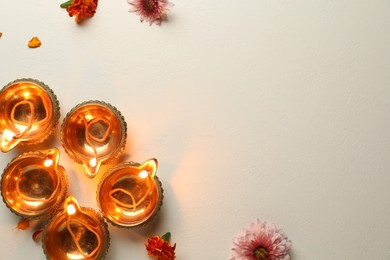 Photo of Diwali celebration. Diya lamps and beautiful flowers on light textured surface, flat lay. Space for text