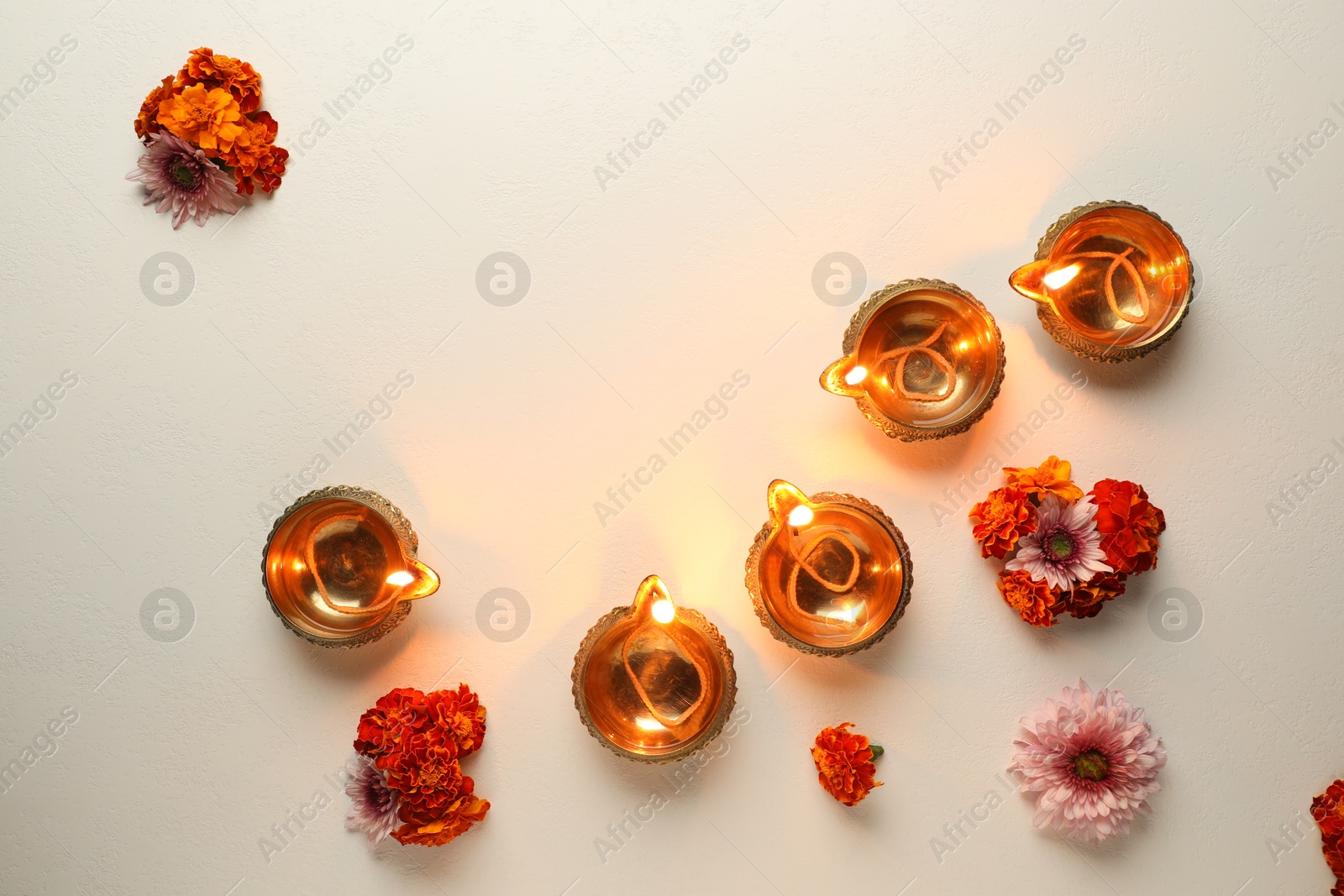 Photo of Diwali celebration. Diya lamps and beautiful flowers on light textured surface, flat lay. Space for text