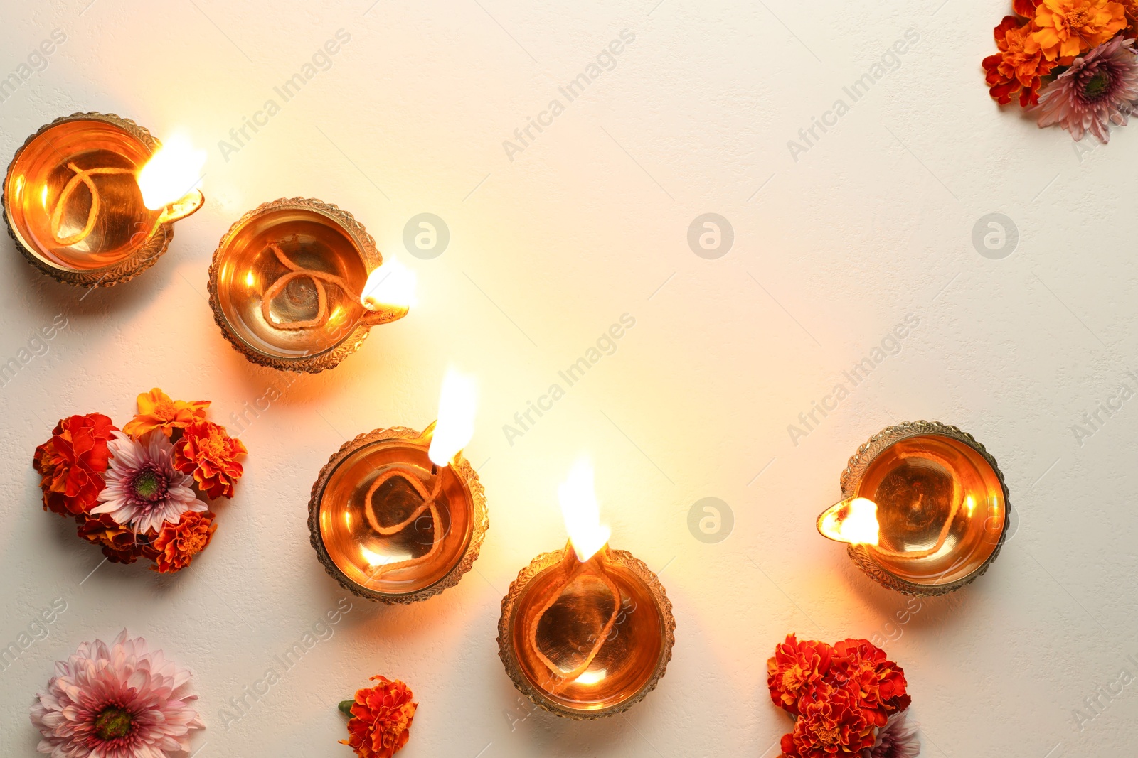 Photo of Diwali celebration. Diya lamps and beautiful flowers on light textured surface, flat lay. Space for text