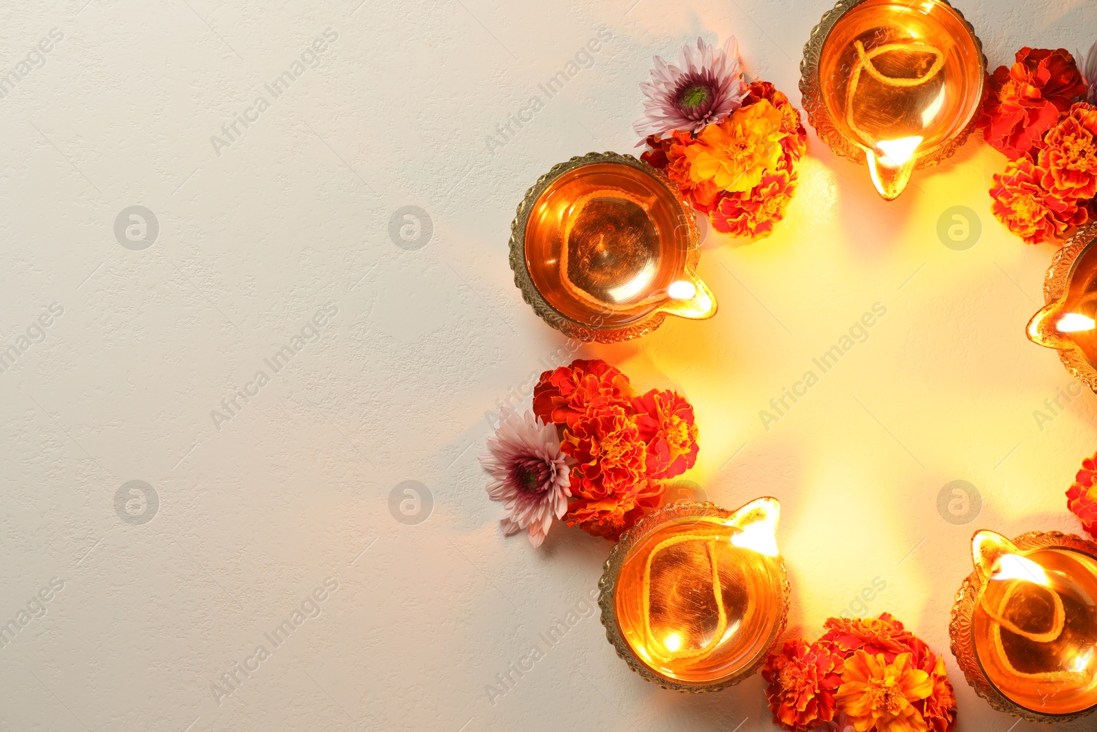 Photo of Diwali celebration. Diya lamps and beautiful flowers on light textured surface, flat lay. Space for text