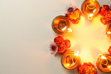 Photo of Diwali celebration. Diya lamps and beautiful flowers on light textured surface, flat lay. Space for text