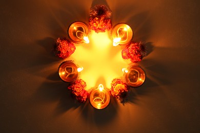 Photo of Diwali celebration. Diya lamps and beautiful flowers on dark textured surface, flat lay. Space for text