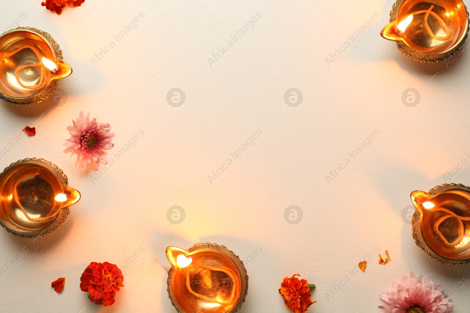 Photo of Diwali celebration. Diya lamps and beautiful flowers on light textured surface, flat lay. Space for text