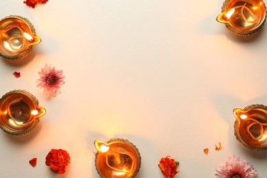 Photo of Diwali celebration. Diya lamps and beautiful flowers on light textured surface, flat lay. Space for text