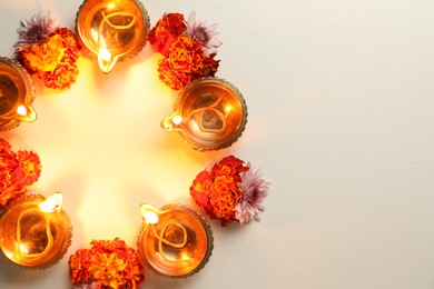 Photo of Diwali celebration. Diya lamps and beautiful flowers on light textured surface, flat lay. Space for text