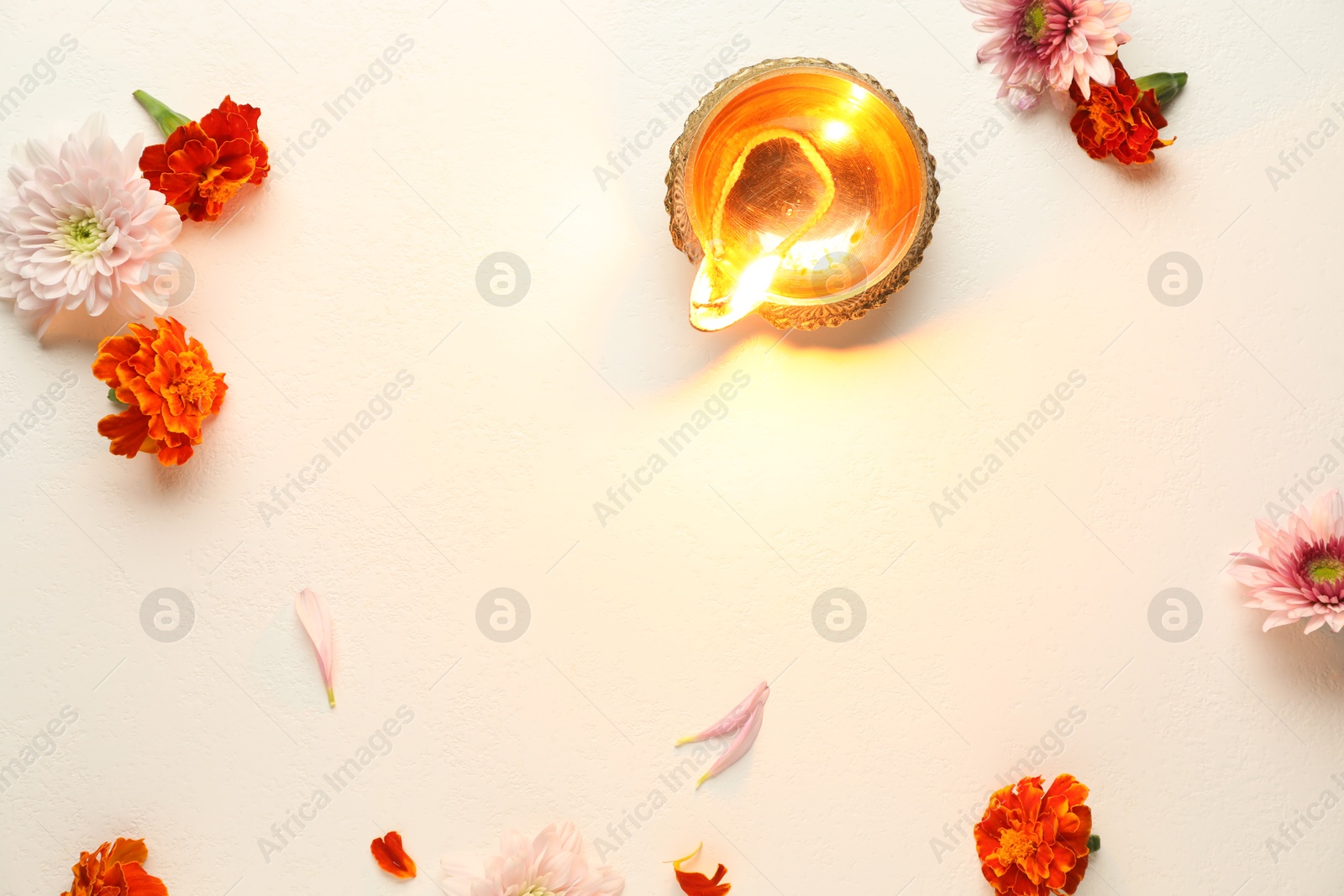 Photo of Diwali celebration. Diya lamp and beautiful flowers on light textured surface, flat lay. Space for text