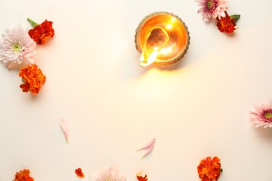 Photo of Diwali celebration. Diya lamp and beautiful flowers on light textured surface, flat lay. Space for text