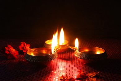 Diwali celebration. Diya lamps and beautiful flowers on dark background, closeup