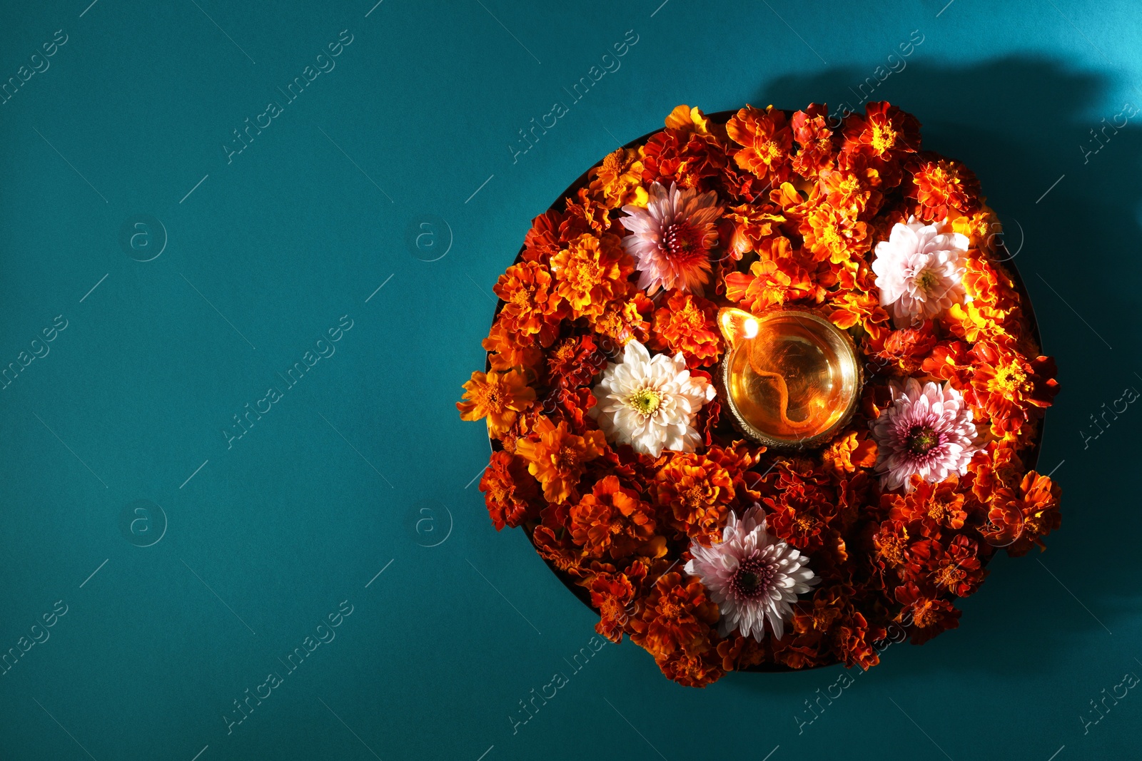 Photo of Diwali celebration. Diya lamp and beautiful flowers on turquoise background, top view. Space for text