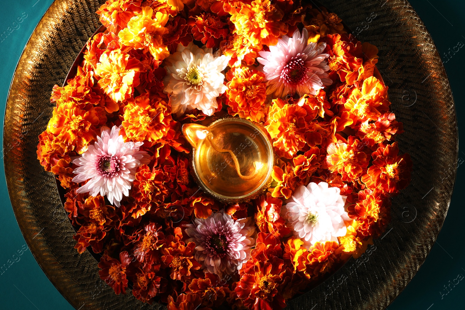 Photo of Diwali celebration. Diya lamp and beautiful flowers on turquoise background, top view