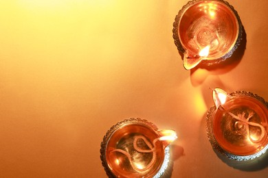 Photo of Diwali celebration. Diya lamps on orange background, flat lay. Space for text