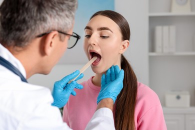 Photo of Doctor examining woman's throat with tongue depressor in clinic