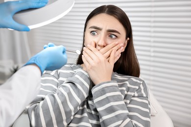 Photo of Dental phobia. Dentist working with scared woman in clinic, closeup