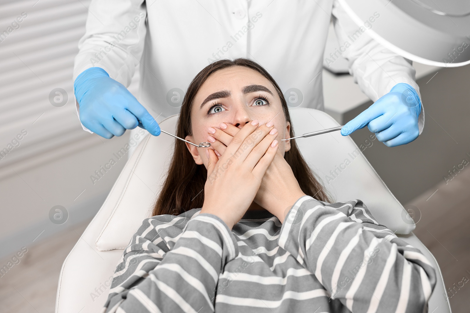 Photo of Dental phobia. Dentist working with scared woman in clinic, closeup