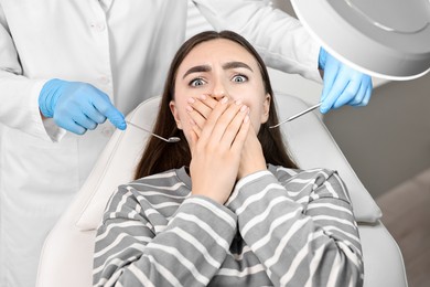 Photo of Dental phobia. Dentist working with scared woman in clinic, above view