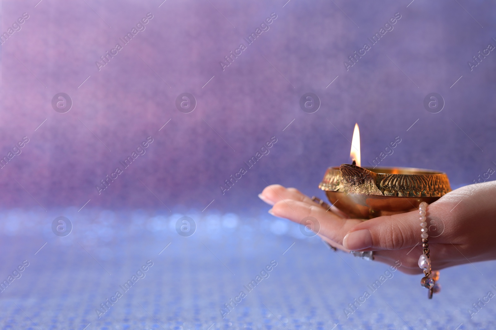 Photo of Diwali celebration. Woman holding lit diya lamp on color background, closeup. Space for text