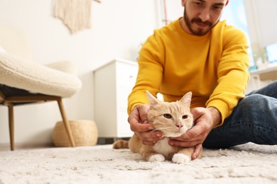 Photo of Man petting cute ginger cat on floor at home, selective focus. Space for text