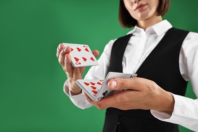 Photo of Professional croupier shuffling cards on green background, closeup