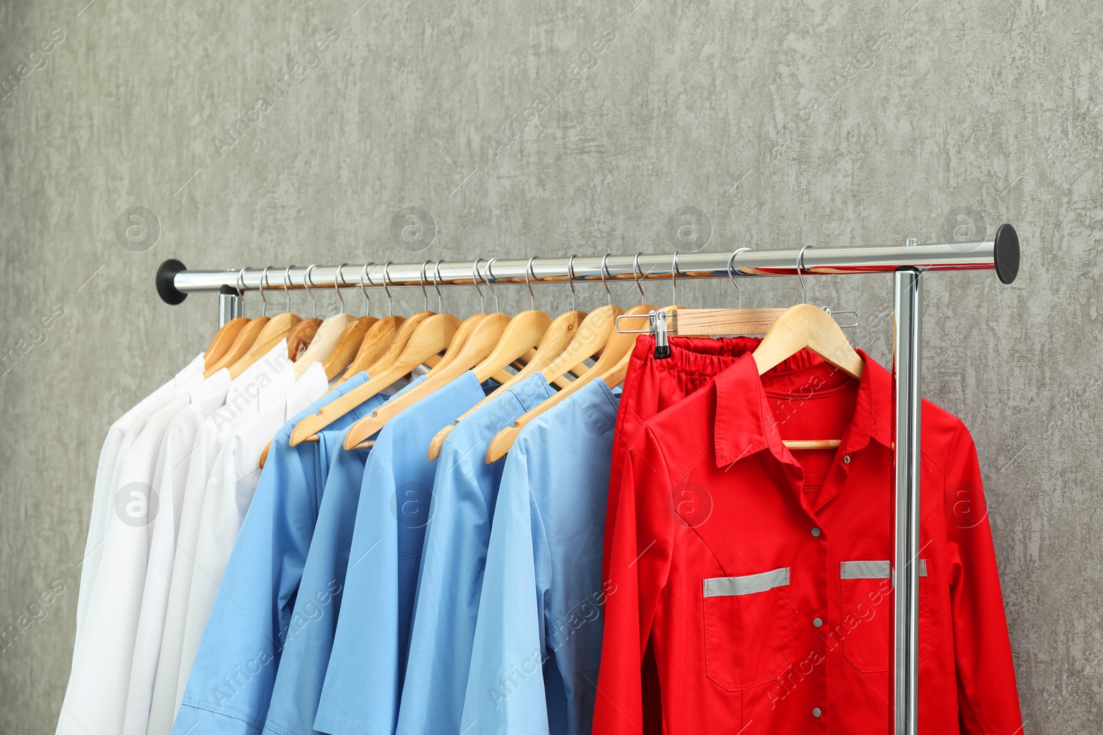 Photo of Different medical workers' uniforms on clothing rack against grey background