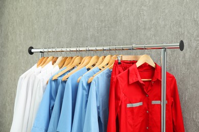 Photo of Different medical workers' uniforms on clothing rack against grey background