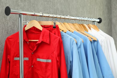 Photo of Different medical workers' uniforms on clothing rack against grey background