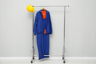 Photo of Worker's uniform and hard hat on clothing rack near grey wall indoors