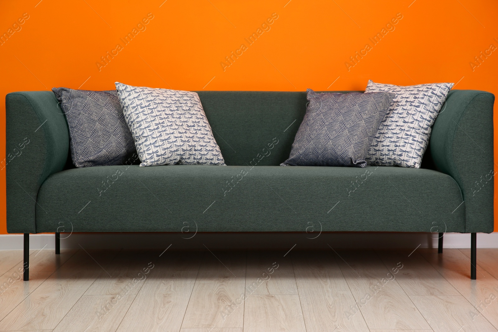 Photo of Stylish sofa with pillows near orange wall indoors