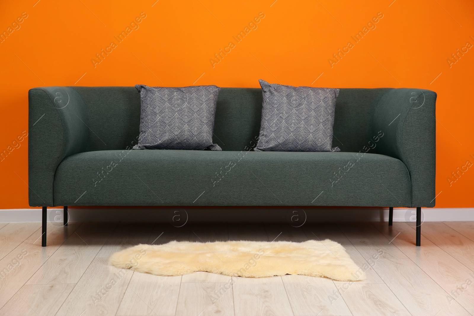 Photo of Stylish sofa with pillows near orange wall indoors