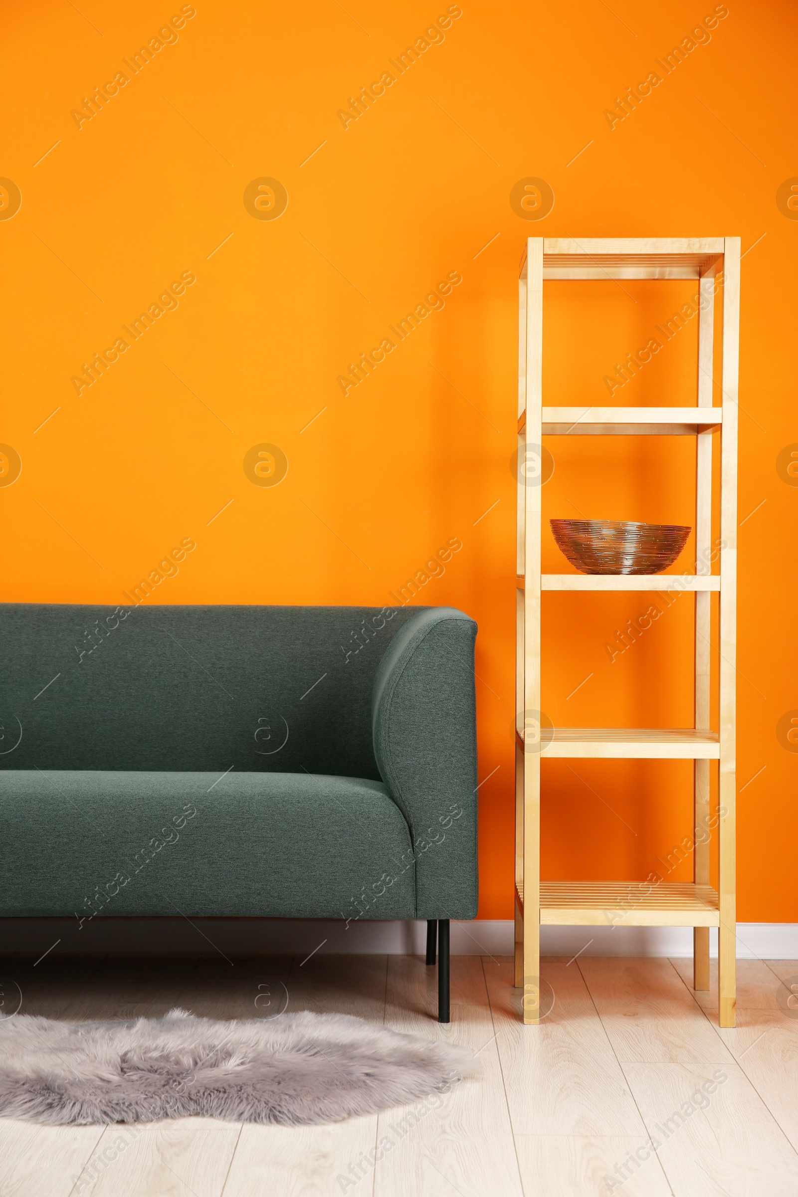 Photo of Stylish sofa and shelving unit near orange wall indoors