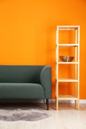 Photo of Stylish sofa and shelving unit near orange wall indoors