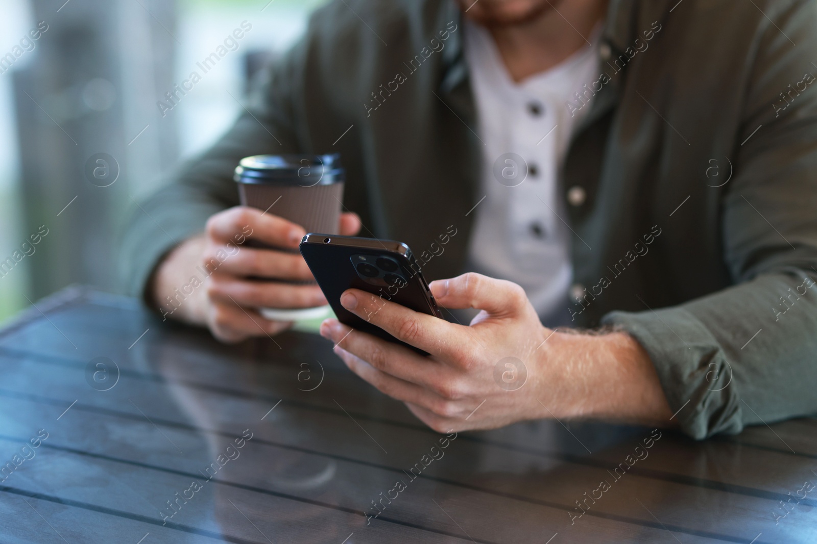 Photo of Man with paper cup using smartphone at outdoor cafe, closeup