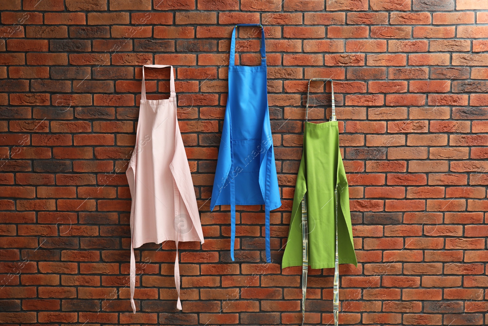 Photo of Many chef's aprons hanging on brick wall