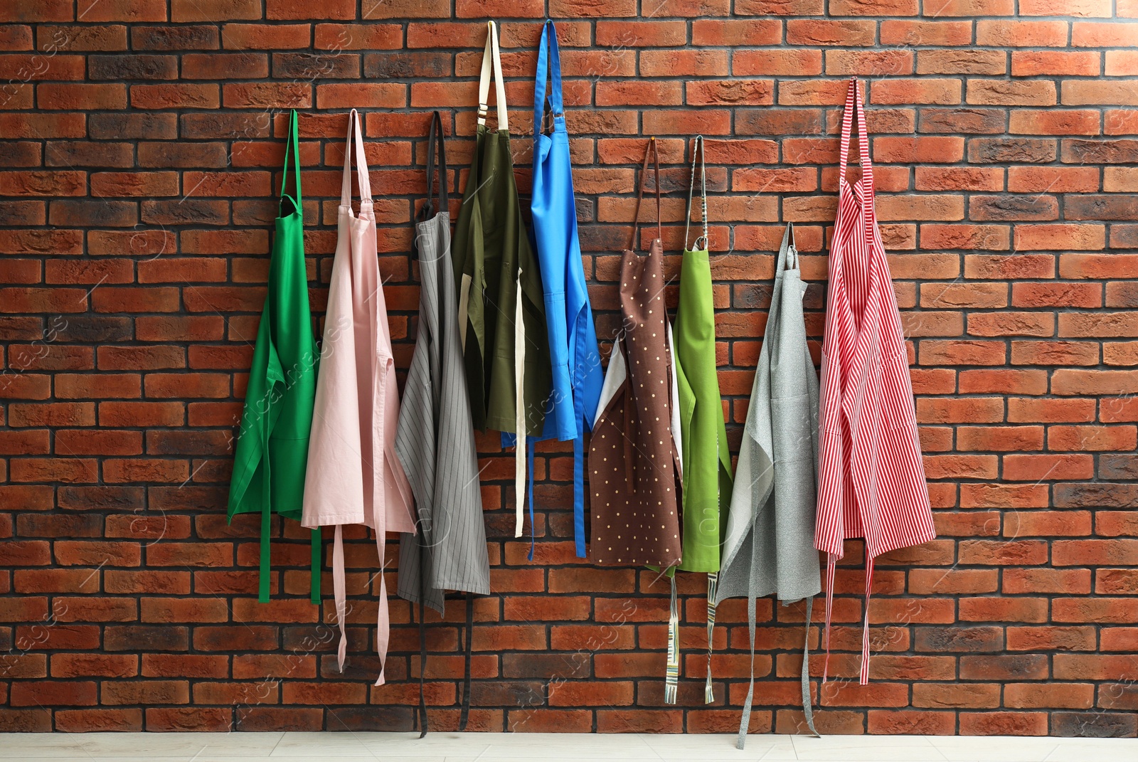 Photo of Many chef's aprons hanging on brick wall