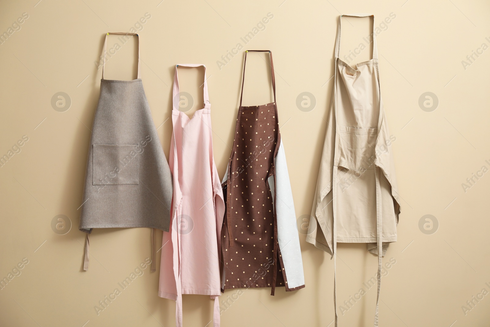 Photo of Many chef's aprons hanging on beige wall